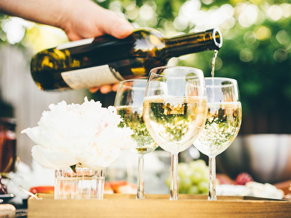 Drei Weingläser auf einem Tisch, die gerade aus einer Flasche gefüllt werden